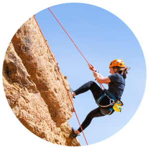 Student in rock climbing gear scales a rock face.